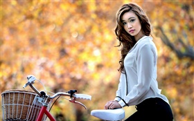 A menina asiática e de bicicleta no Outono