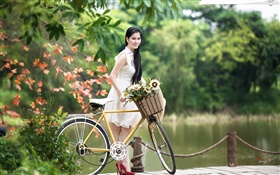 Sorriso asiático da menina, vestido branco, bicicleta, parque